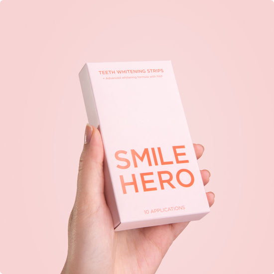 Girl holding Smile Hero's Teeth Whitening Strips behind a pink background at home