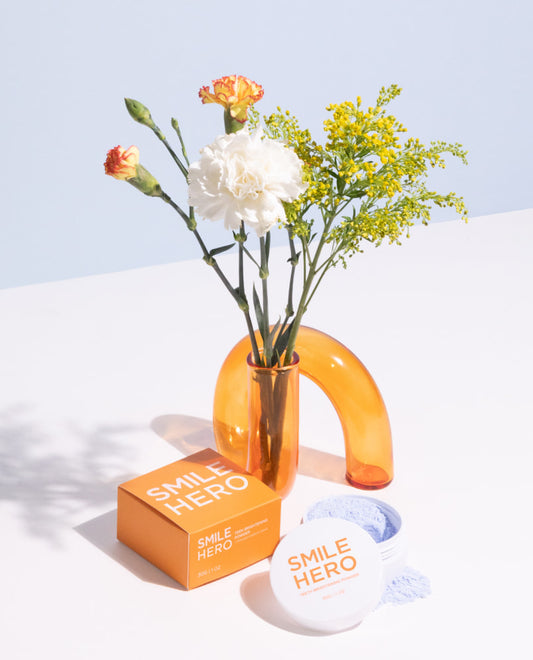 Smile Hero's Teeth Brightening Powder opened and about to be used in front of natural flowers